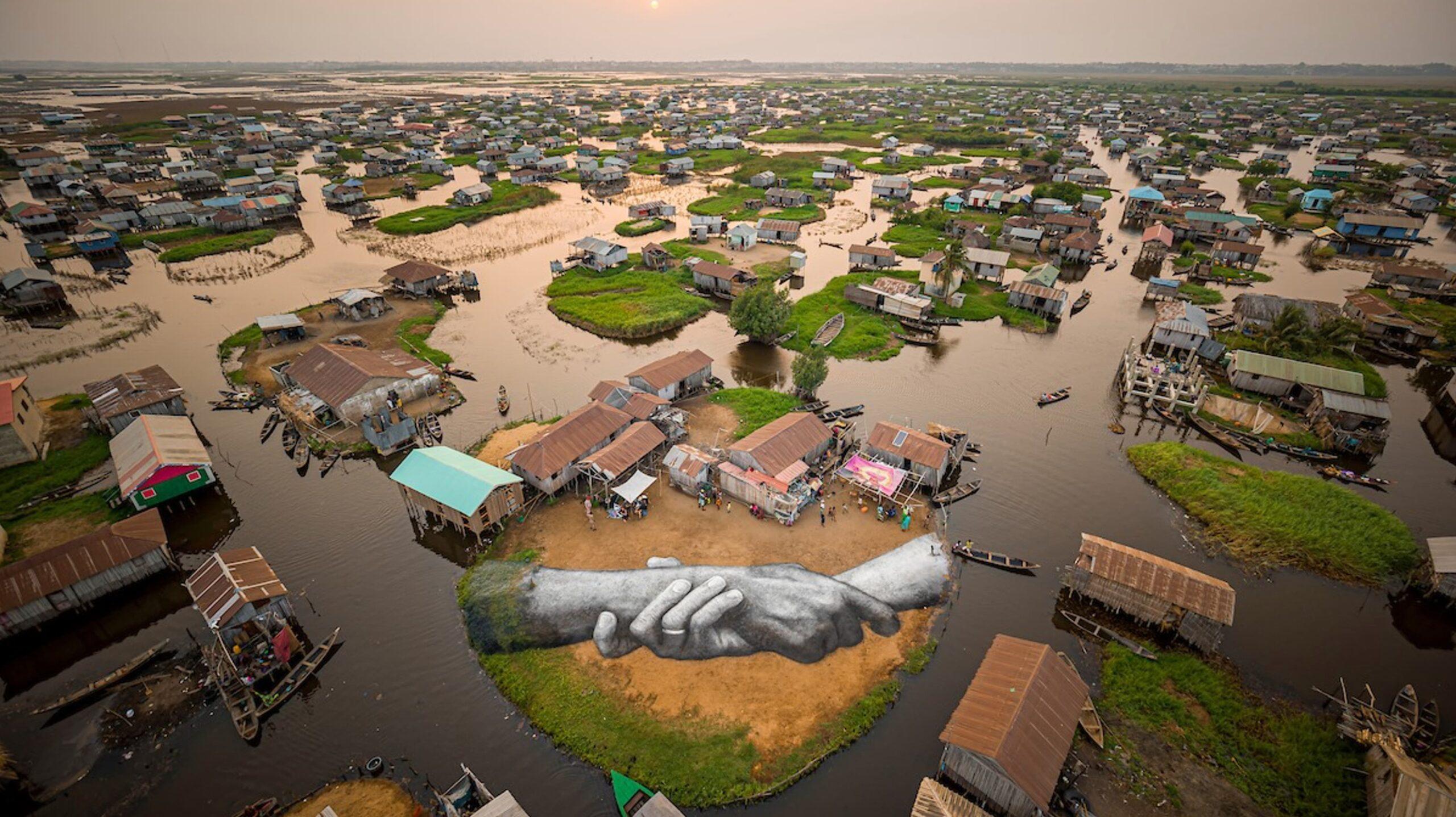 Oeuvre de landart réalisée par Saype dans le village lacustre de Ganvié au Bénin représentant deux mains qui se tiennent.
