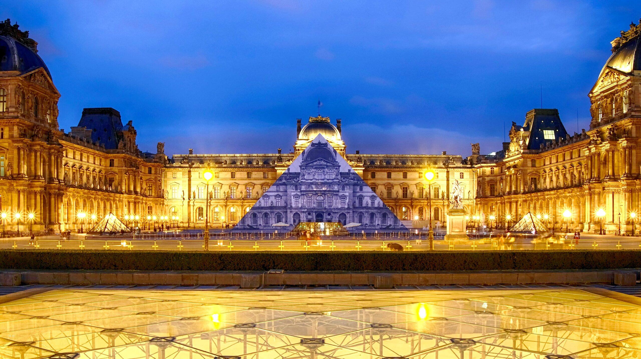 La pyramide du Louvre est recouverte d'une photo de l'artiste JR qui la fait se confondre avec l'arrière plan depuis un point donné.