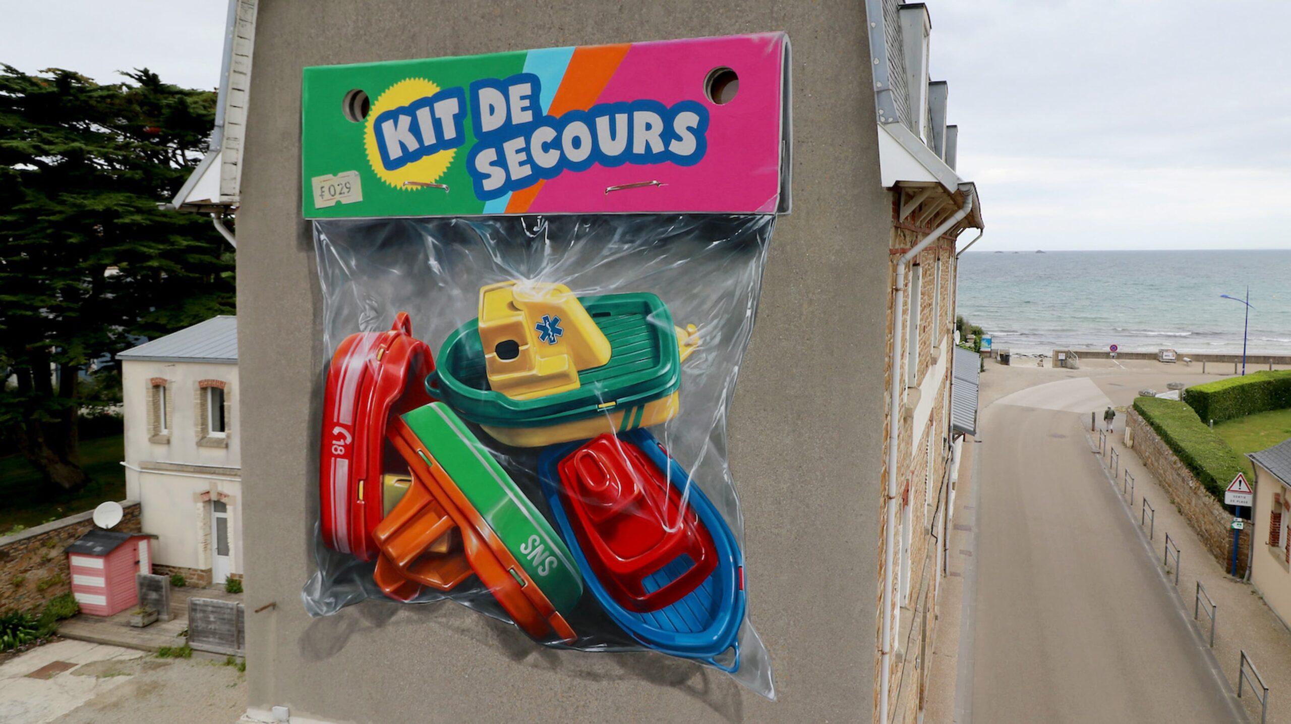 Oeuvre murale réalisée sur le mur d'une maison bretonne en bord de mer représentant un sachet de jouets en plastiques, 4 petits bateaux, et intitulée "Kit de secours".