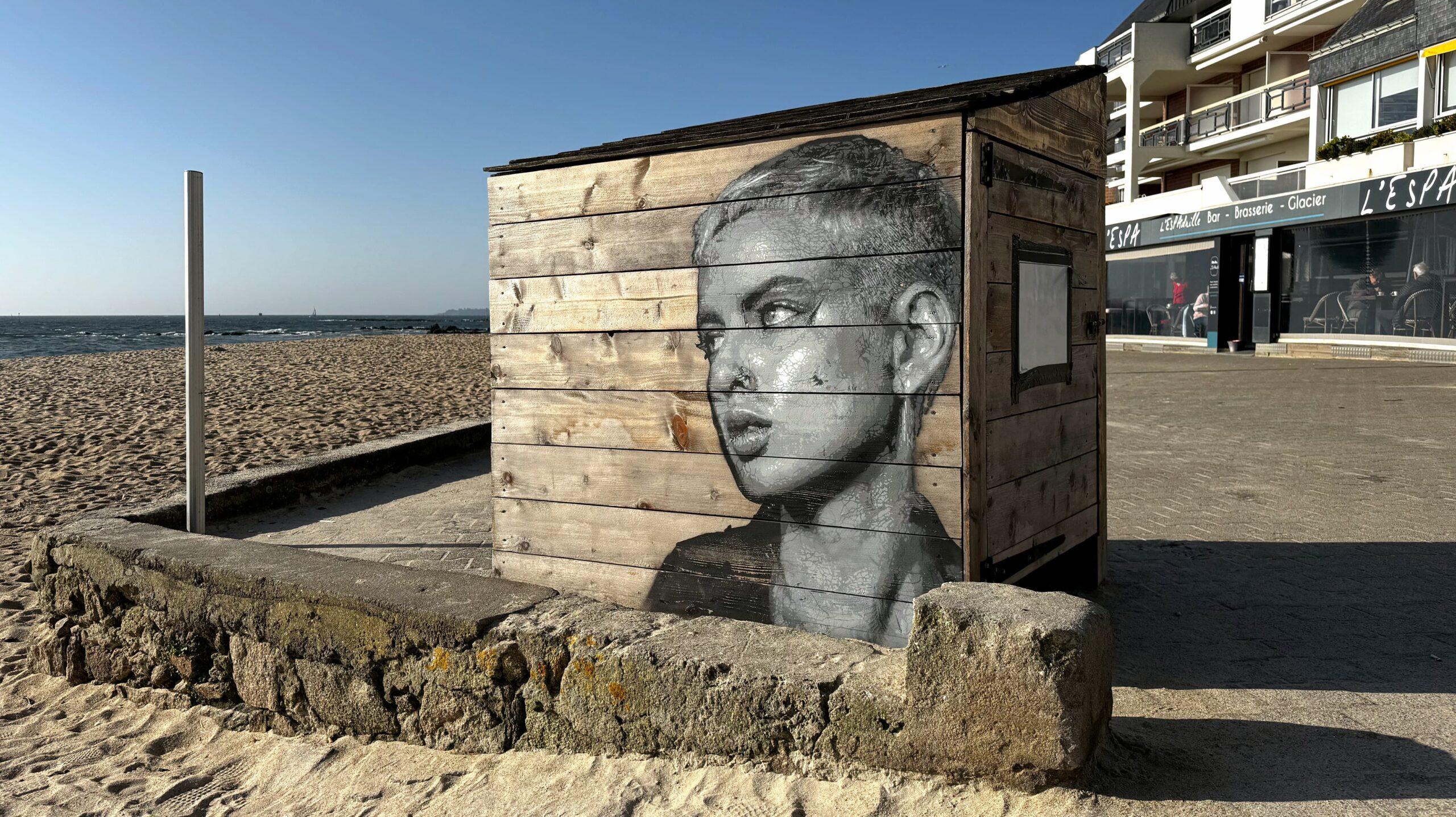 Portrait au pochoir d'une jeune femme aux cheveux courts. L'oeuvre a été réalisée par le street artiste Kelu Abstract en bord de mer et la jeune femme regarde vers le large.